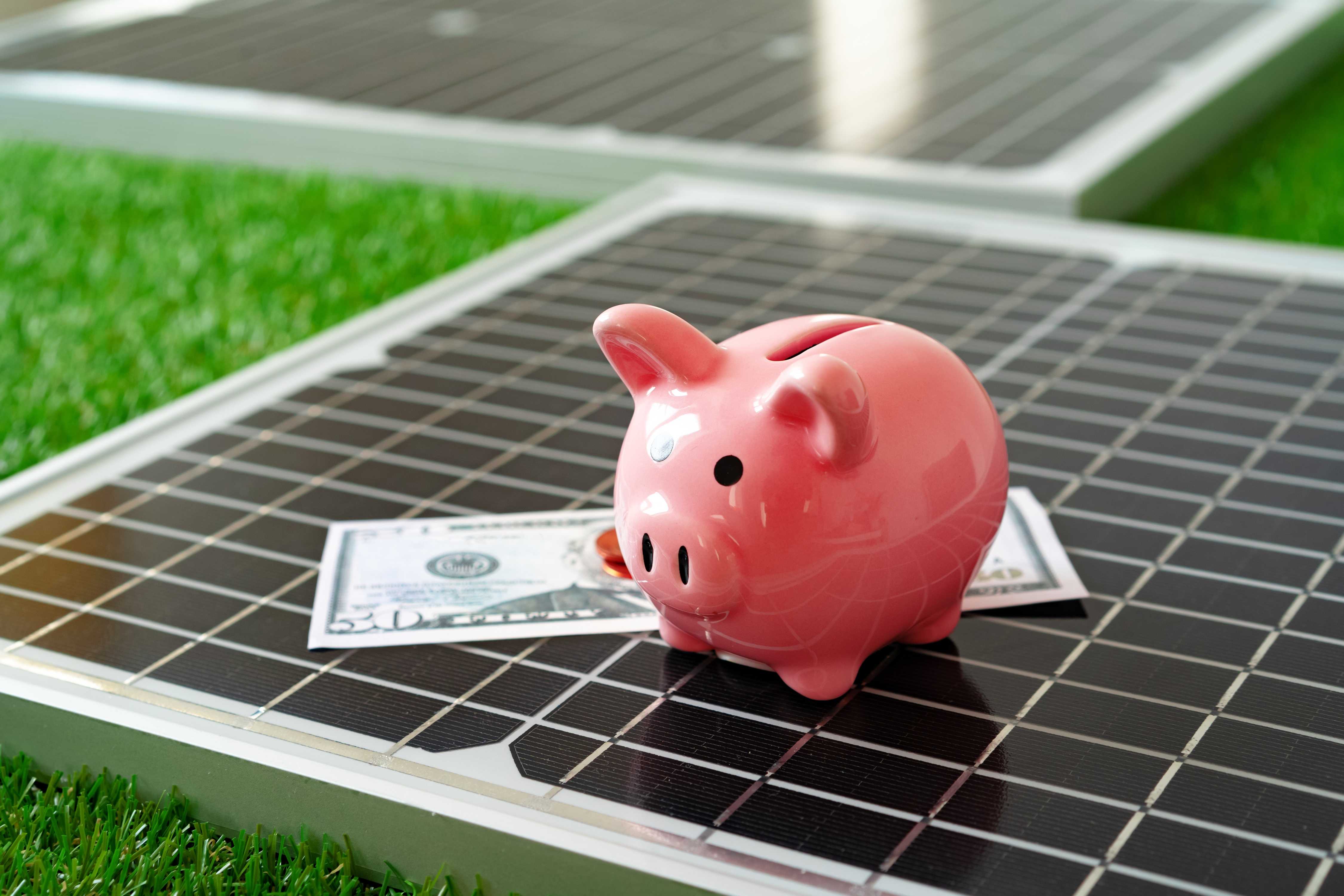 piggy bank and a dollar on top of a solar panel