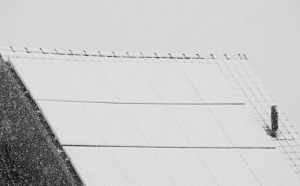 snow-covered solar panels on a rooftop producing power in winter