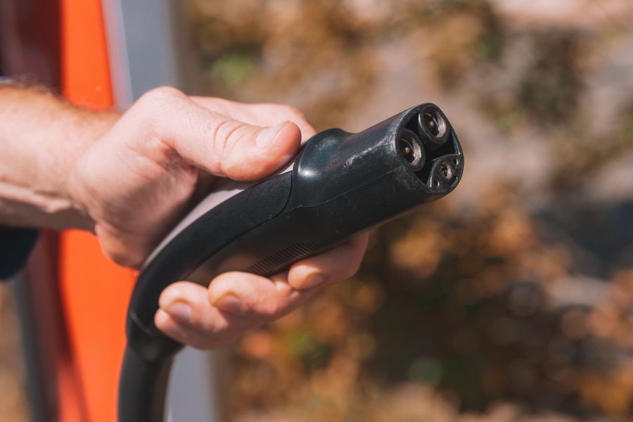 hand plugging a charging cable into an electric vehicle at home